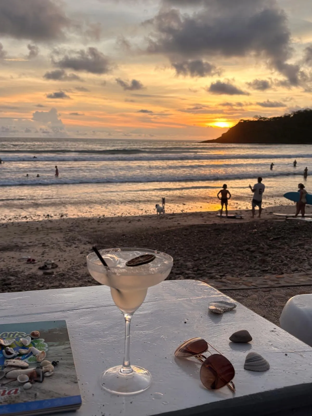 Sunset over Playa El Remanso with surfers in the water and a drink on a beachfront table